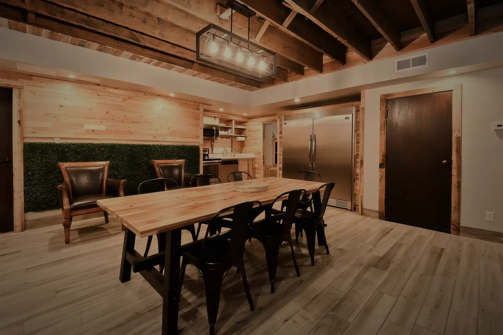 The long table under exposed timber beams, the kitchen behind it.